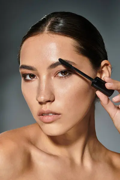 A beautiful woman focuses intently while applying brow gel to her eyebrows indoors. — Stock Photo