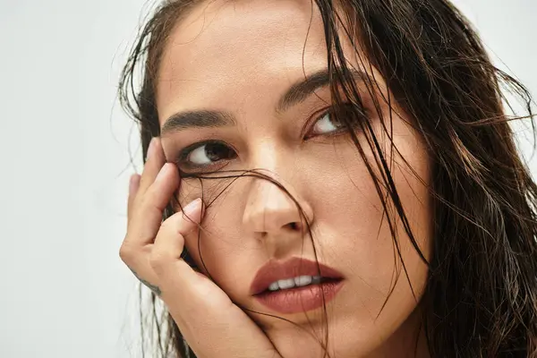 Une belle femme touche doucement son visage tandis que ses cheveux mouillés encadrent ses traits. — Photo de stock
