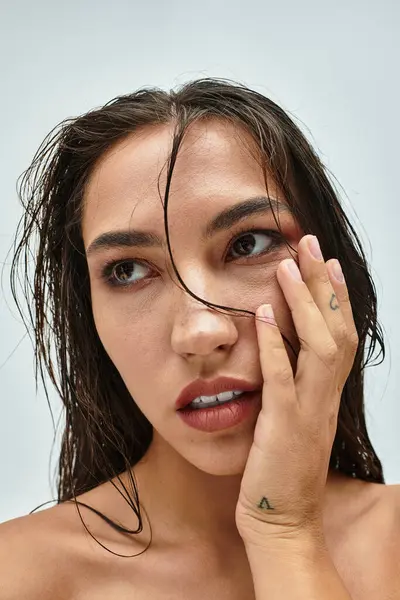 La mujer muestra una mirada expresiva mientras toca suavemente su rostro, destacando su belleza. - foto de stock