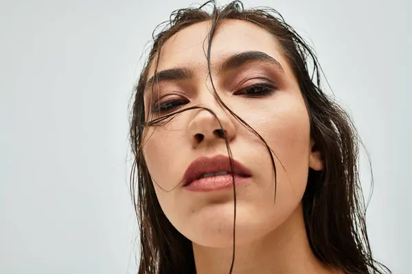 The lovely woman gazes confidently with wet hair framing her face, showcasing her artistic makeup. — Stock Photo
