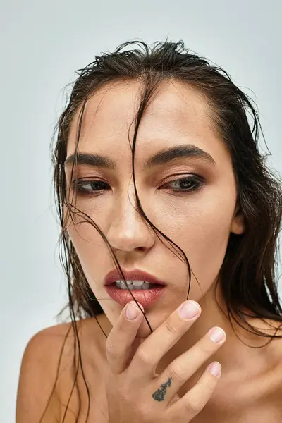 A stunning close up of a woman with long wet hair thoughtfully brushing her face. — Stock Photo