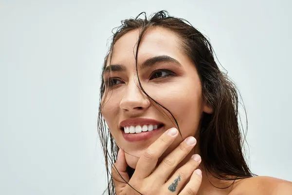 Brillanti sorrisi si irradiano da una donna con i capelli bagnati mentre si tocca scherzosamente il viso dolcemente.. — Foto stock