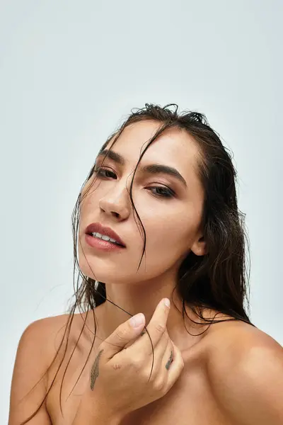 A stunning woman poses with wet hair, gently touching her face against a light background. — Stock Photo