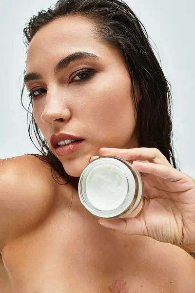 Esta mulher deslumbrante destaca sua pele radiante enquanto segura um creme nutritivo suavemente. — Fotografia de Stock