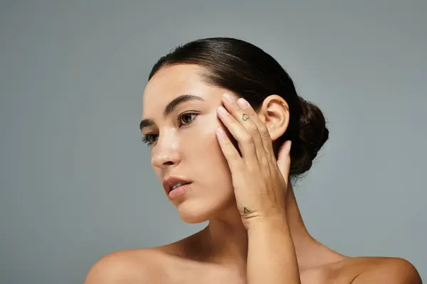 Uma mulher bonita delicadamente acaricia seu rosto, destacando suas características elegantes e graça. — Fotografia de Stock