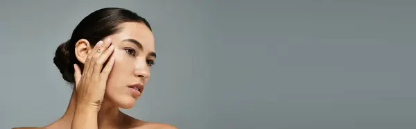 Uma mulher bonita habilmente acaricia sua bochecha enquanto exala elegância em uma atmosfera calma. — Fotografia de Stock