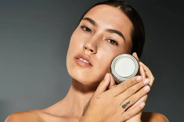 A woman gently holds a skincare jar while highlighting her glowing complexion in warm lighting. — Stock Photo