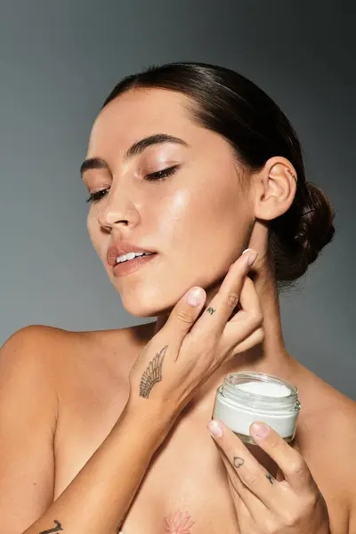 Eine Frau trägt im Atelier sanft Creme mit nachdenklichem Gesichtsausdruck auf ihre Haut auf. — Stockfoto
