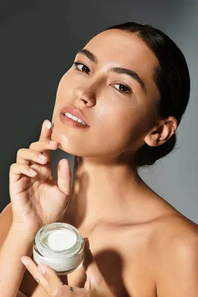 The woman delicately applies cream to her face, radiating confidence and beauty. — Stock Photo
