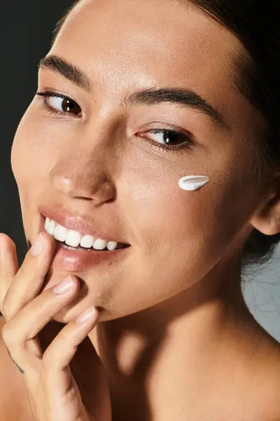 A woman with a radiant smile applies cream to her face while enjoying a moment of self care. — Stock Photo