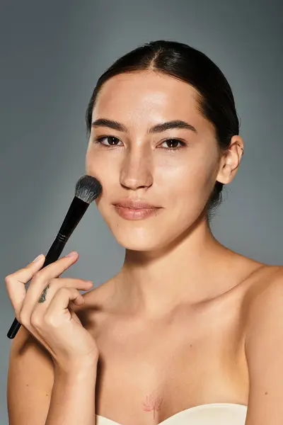 A woman enjoys applying makeup, enhancing her natural beauty with a brush in the studio light. — Stock Photo