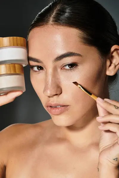 The woman highlights skincare jars and expertly applies makeup with a brush, exuding confidence. — Stock Photo