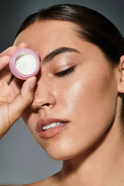 A beautiful woman gently applies moisturizer to her skin, embracing a moment of self care. — Stock Photo