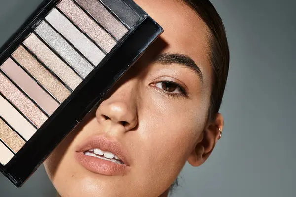 A mulher posa elegantemente com uma paleta de maquiagem, destacando suas características em luz suave.. — Fotografia de Stock
