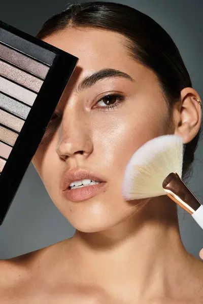 A beautiful woman enhances her features using a makeup palette and brush in a chic atmosphere. — Stock Photo