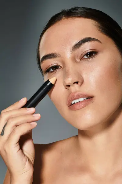The woman applies concealer to accentuate her features, showcasing a serene expression. — Stock Photo