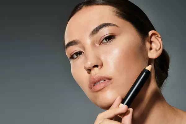 A beautiful woman enhances her features with a makeup tool while posing confidently. — Stock Photo