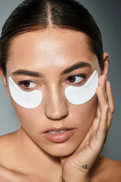 A beautiful woman gently applies under eye patches while preparing for a skincare ritual. — Stock Photo