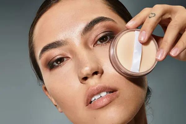 Una mujer hermosa realza sus rasgos mientras sostiene un polvo compacto cerca de su cara. - foto de stock