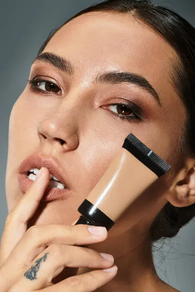 The beautiful woman delicately applies foundation while showcasing her flawless skin. — Stock Photo