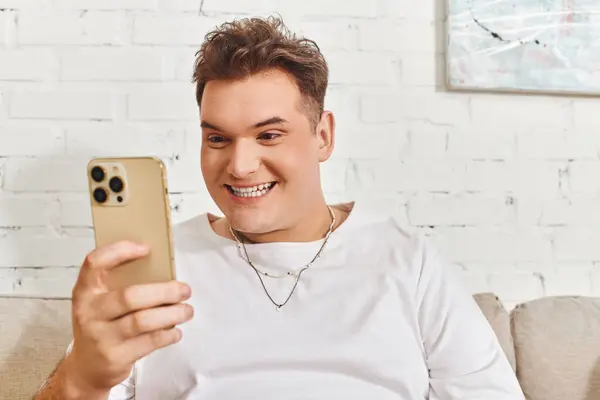 Веселый странный человек ярко улыбается, глядя на свой смартфон в уютной обстановке. — стоковое фото