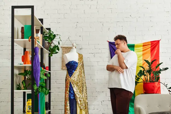 A thoughtful queer person examines a dazzling outfit amidst colorful decor and plants. — Stock Photo