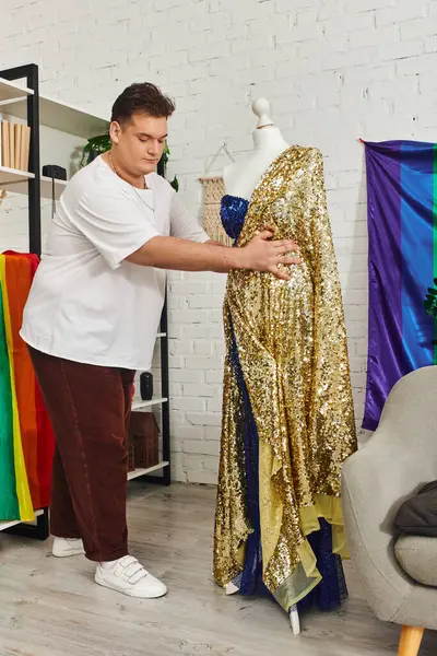 A creative queer person works on a shimmering golden gown surrounded by colorful fabrics. — Stock Photo