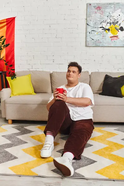 Relaxing on the floor, a queer individual savors a delightful drink in a modern space. — Stock Photo