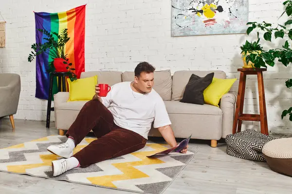A queer person relaxes on a rug while sipping coffee and reading a magazine in a vibrant space. — Stock Photo