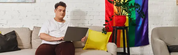 A queer individual sits comfortably on a sofa, using their laptop in a colorful living space. — Stock Photo
