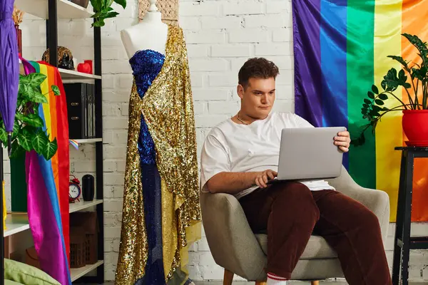 Une personne queer s'assoit dans une chaise élégante, concentrée sur son ordinateur portable dans un cadre dynamique et artistique. — Photo de stock