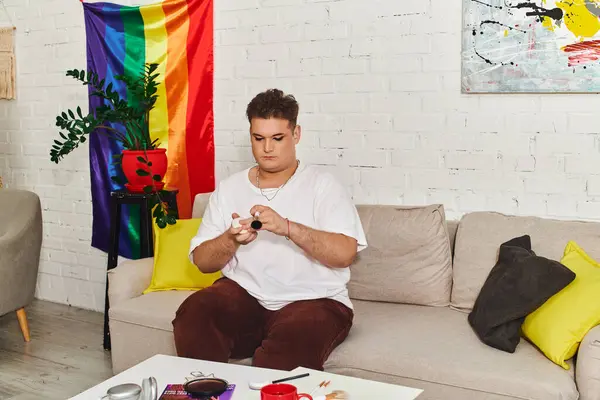Una persona queer está aplicando hábilmente maquillaje en un acogedor, colorido orgullo temático espacio de vida. - foto de stock