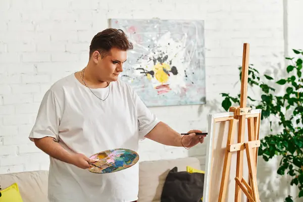 An artist holds a palette filled with colors while focused on painting on a canvas. — Stock Photo