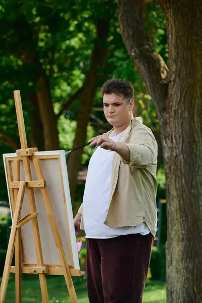 A queer individual focuses on painting with a brush in a serene natural setting. — Stock Photo