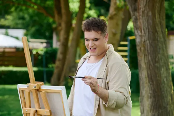 A queer individual happily paints on an easel, enjoying the sunny day in a park. — Stock Photo
