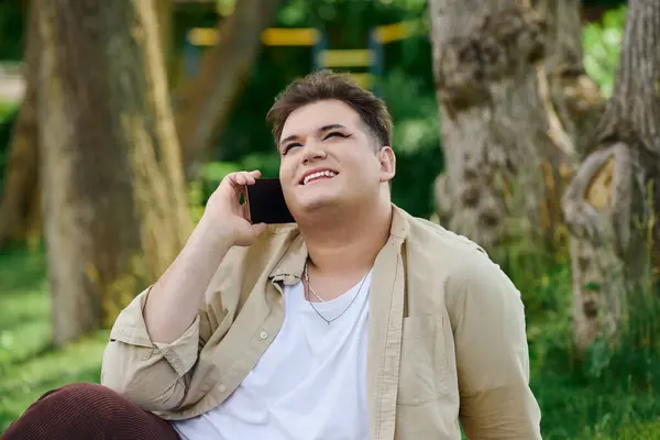 A cheerful individual engages in a lighthearted phone call while seated on lush grass. — Stock Photo