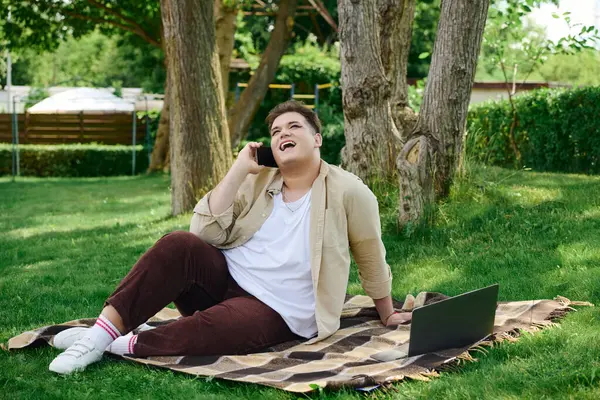 In a lush garden, a queer person sits on a blanket, cheerfully chatting on the phone. — Stock Photo