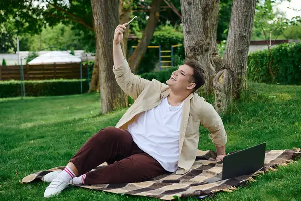 Una persona gay allegra si sdraia su una coperta nel parco, catturando un selfie gioioso. — Foto stock