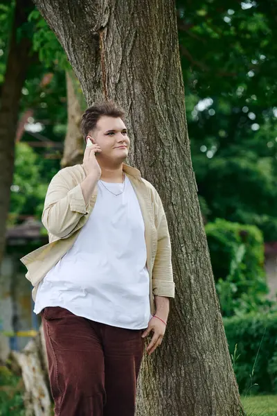 De pé sob uma grande árvore, um indivíduo queer desfruta de um momento de silêncio perdido na música e reflexão. — Fotografia de Stock