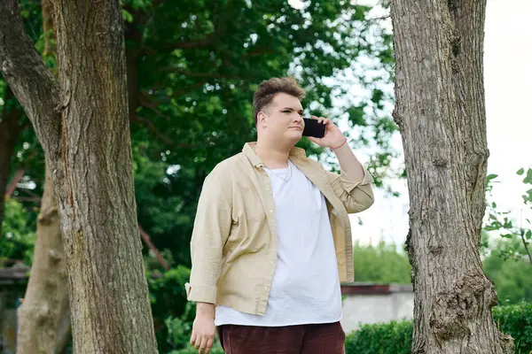 A queer individual chats on the phone in a lively, green outdoor setting. — Stock Photo