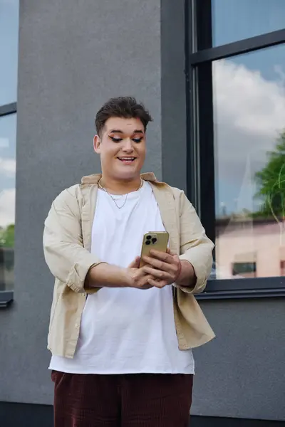Un individuo gay alegre sonríe brillantemente mientras interactúa con su teléfono inteligente fuera. - foto de stock