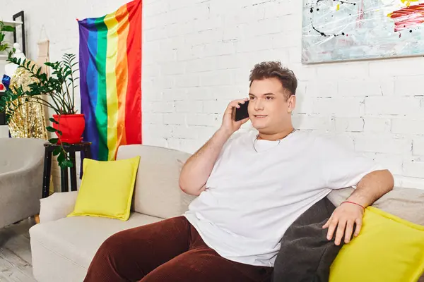 Una persona queer se relaja en un sofá, charlando en el teléfono en medio de una decoración colorida. - foto de stock