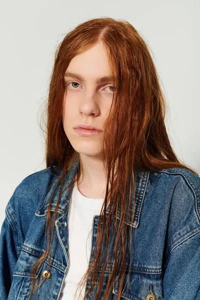 A teenage boy showcases his long red hair and denim outfit while expressing his unique style in the studio. — Stock Photo