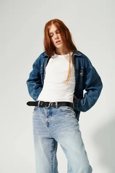 A teenage boy with striking long red hair showcases a trendy denim outfit in a sleek studio environment. — Stock Photo