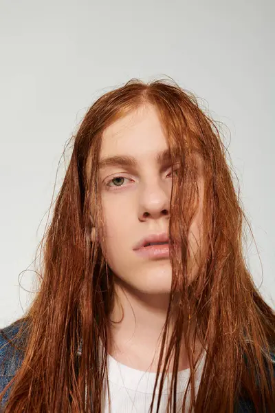 A teenage boy showcases his long red hair and denim outfit while posing confidently in a studio. — Stock Photo
