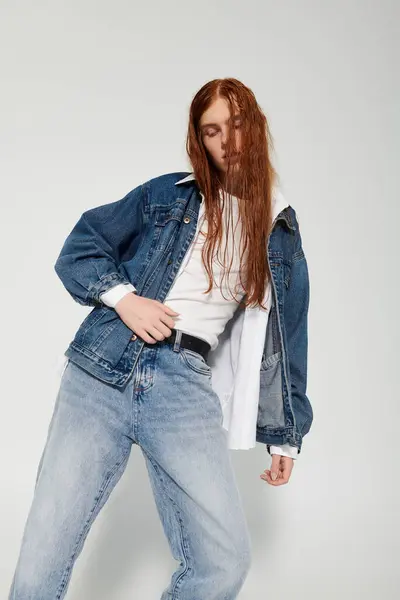 Un adolescent pose avec confiance dans une tenue denim tendance, mettant en valeur ses longs cheveux roux dans un studio dynamique. — Photo de stock