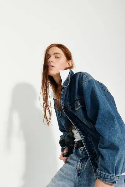 A teenage boy showcases his long red hair and trendy denim outfit in a bright studio environment. — Stock Photo