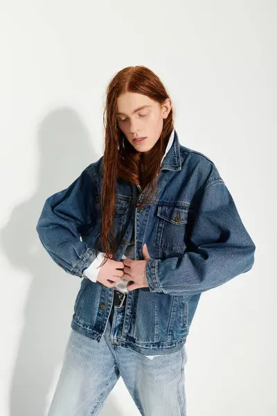 Un adolescent met en valeur ses longs cheveux roux et sa tenue denim tendance tout en posant en toute confiance dans un studio. — Photo de stock