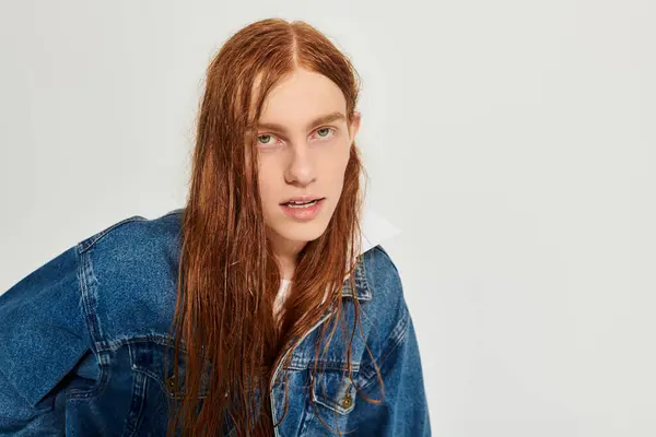 A teenage boy with striking long red hair poses stylishly in a denim outfit against a neutral backdrop. — Stock Photo