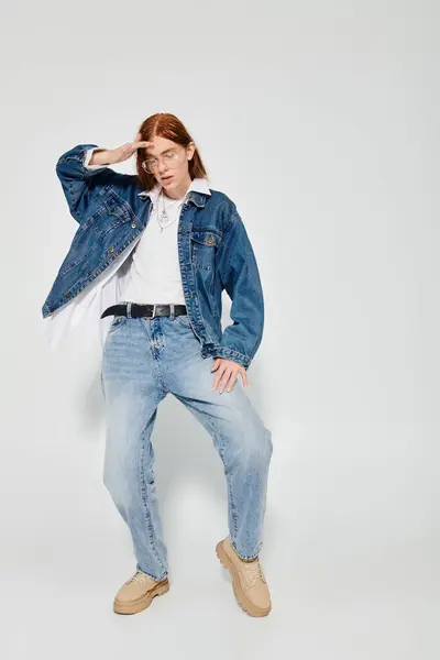 Ein halbwüchsiger Junge zeigt seine langen roten Haare und Jeans und posiert in einem Atelier in modischer Pose. — Stockfoto